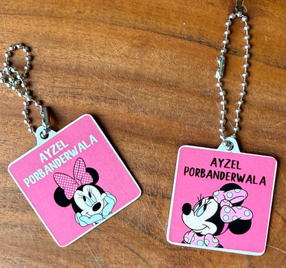Two pink square bag tags with silver ball chains, featuring a Minnie Mouse-style character illustration 