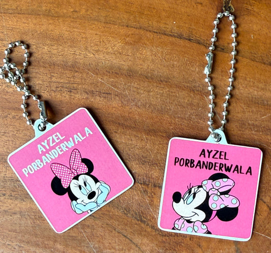 Two pink square bag tags with silver ball chains, featuring a Minnie Mouse-style character illustration 