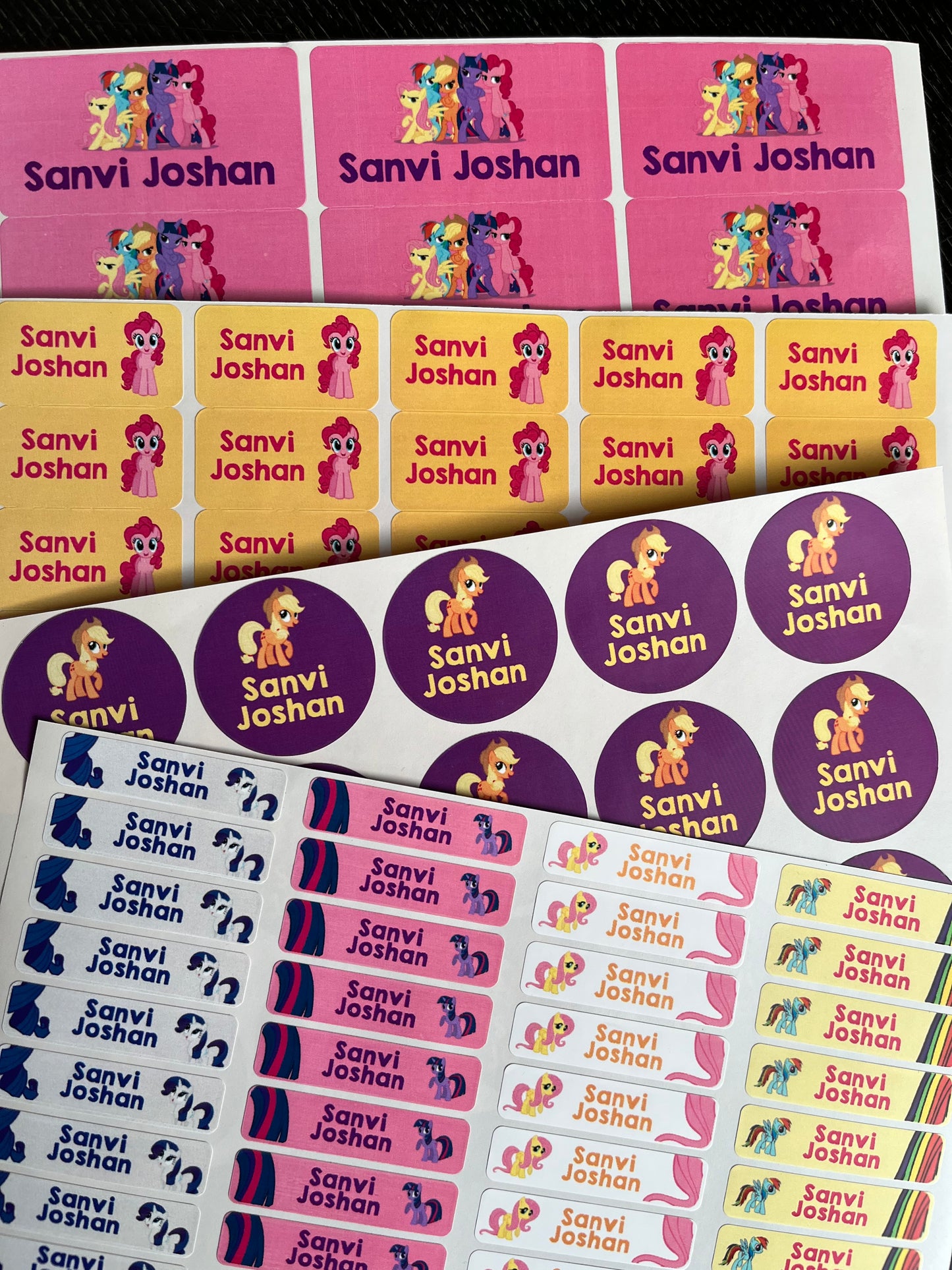 Custom printed sticker sheets featuring cartoon pony characters and the names 'Sanvi Joshan' in multiple colorways, including pink, yellow, purple, and blue.