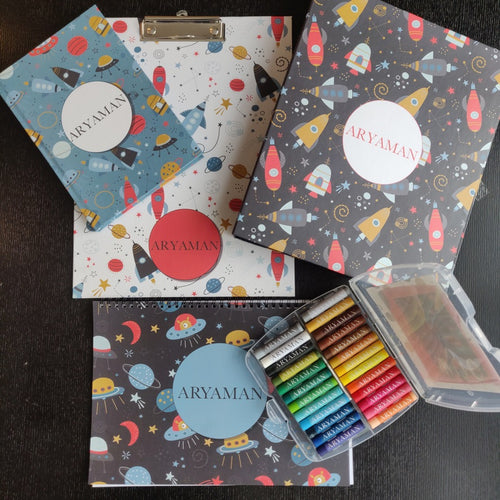 a set of 5 items clipboard notebook folder art book and box of personalised crayons with a space travel theme featuring spaceships, rockets planets and starts