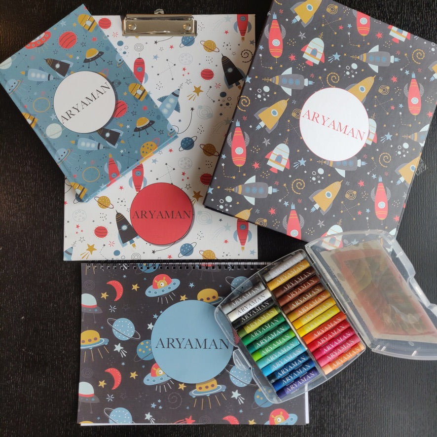 a set of 5 items clipboard notebook folder art book and box of personalised crayons with a space travel theme featuring spaceships, rockets planets and starts