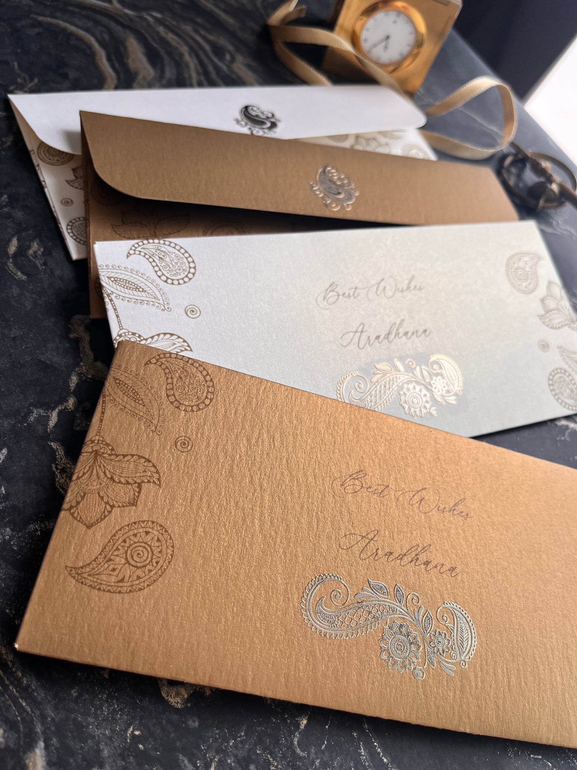Three decorative envelopes with paisley patterns on a textured surface.