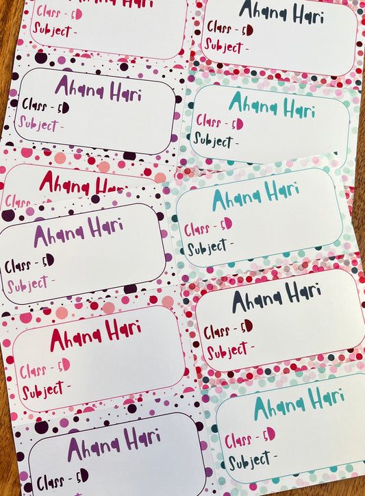 A set of printed class roster labels or name tags laid out on a wooden surface. Each label has a white rounded rectangle body with a decorative border of pink, purple, and teal polka dots on a white background.