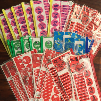Assorted colorful name labels in various shapes and designs, primarily in pink, yellow, red, green, blue, and white, displayed on a table.