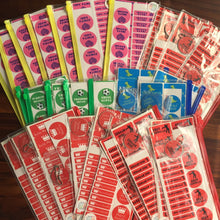 Assorted colorful name labels in various shapes and designs, primarily in pink, yellow, red, green, blue, and white, displayed on a table.