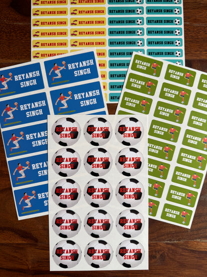 personalised, waterproof school name labels  soccer player graphics, alongside sheets of round football themed stickers and a sheet of rectangular name stickers, all arranged on a dark wood background.