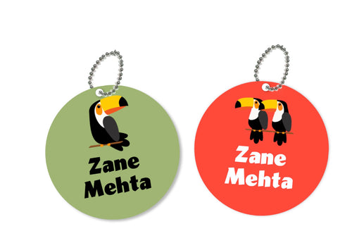 Two round metal bag tags with a toucan design, one green and one red, both with the name 'Zane Mehta' printed on them.