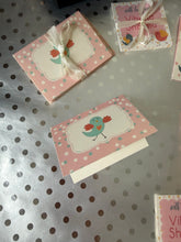 Small pink cards with decorative elements on a metallic surface with polka dot pattern