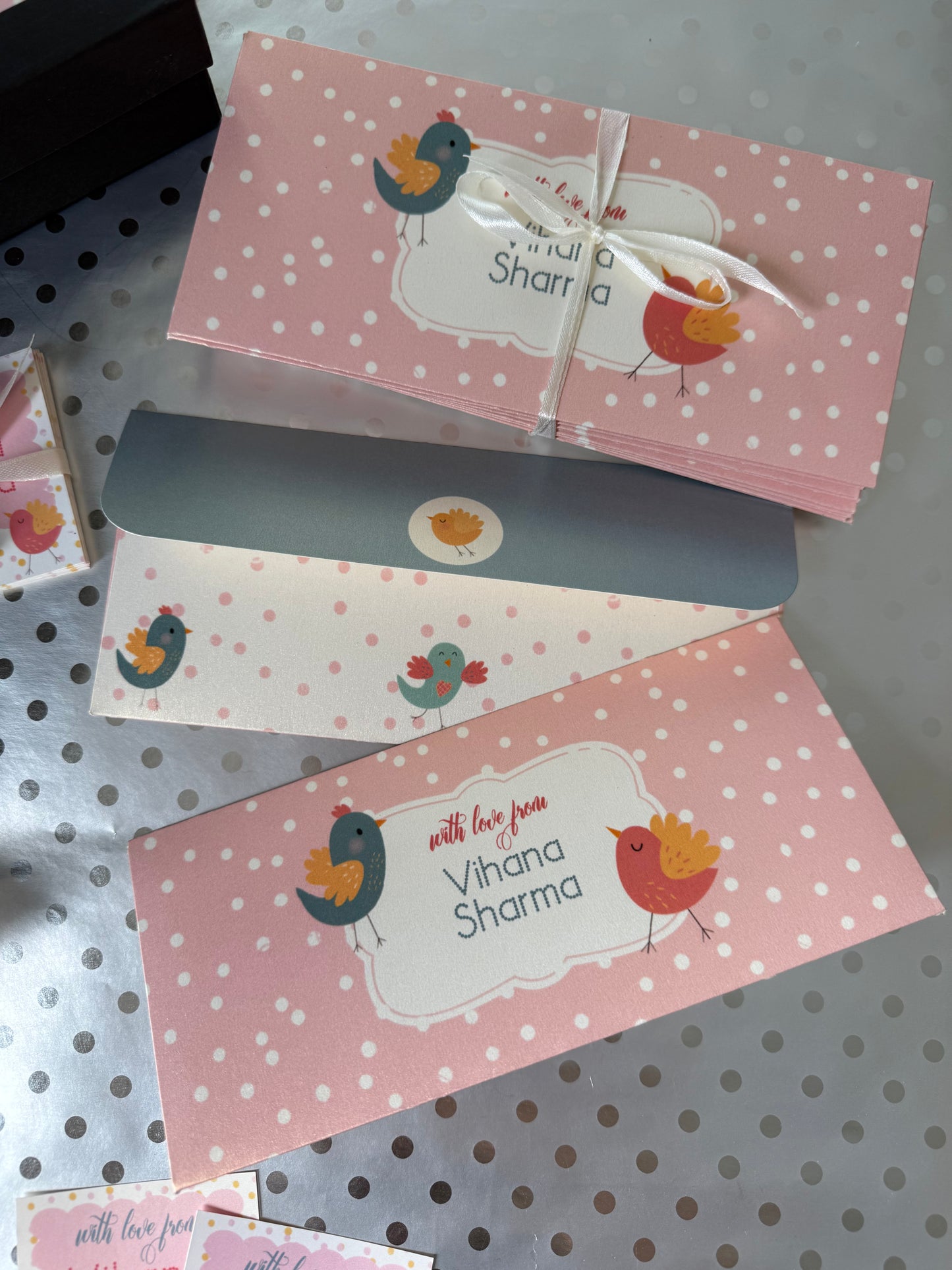 Two pink gift envelopes with polka dots and a name on a gray surface.