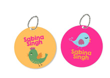 Two round metal bag tags with a bird theme. One is pink with a blue bird and the other is green with a yellow bird.