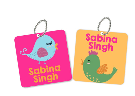 Two square metal bag tags with a bird theme. One is pink with a blue bird and the other is green with a yellow bird.