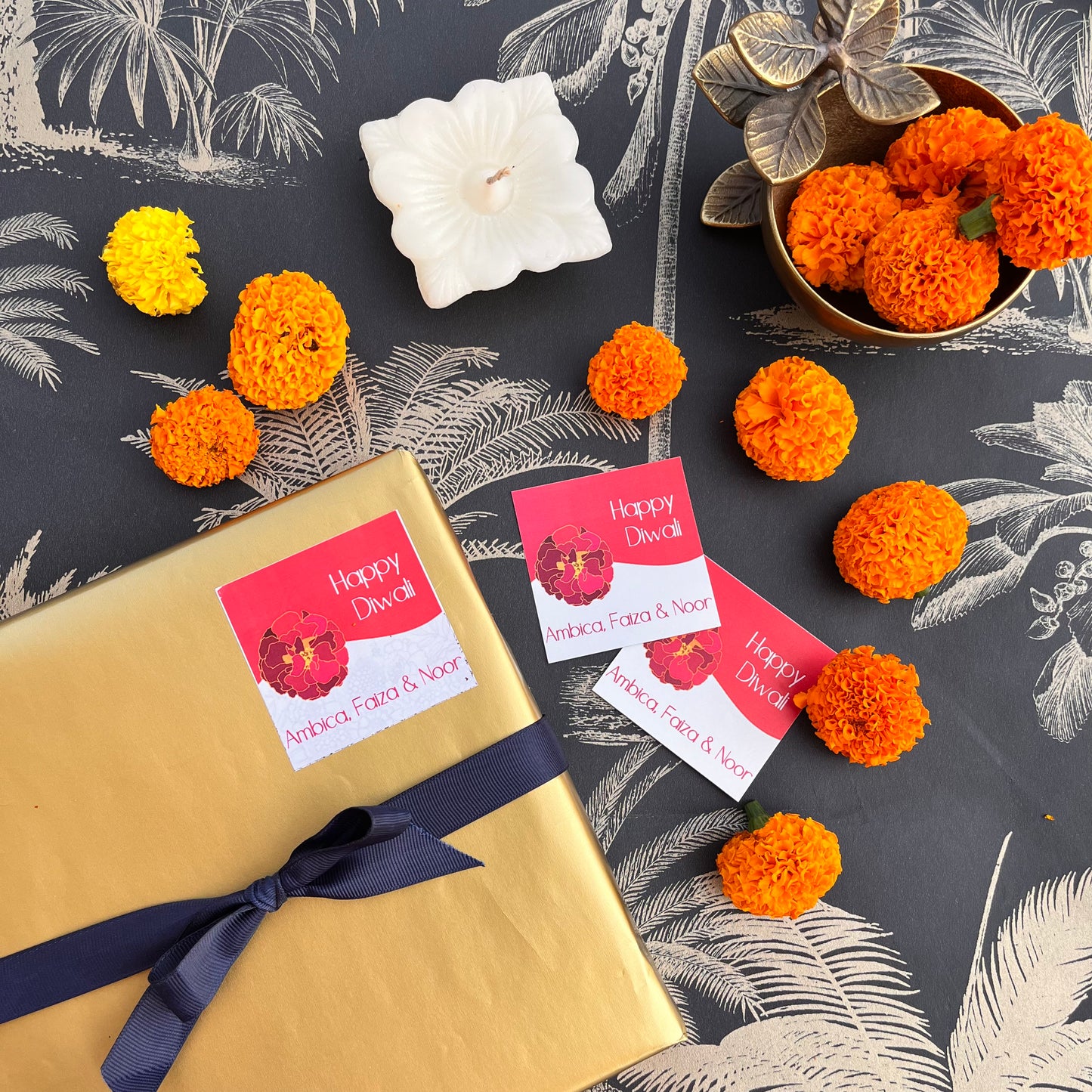 Gift tags with 'Happy Diwali' and 'Happy New Year' text, presented on a gift wrapped in gold paper, alongside orange decorations and a candle.