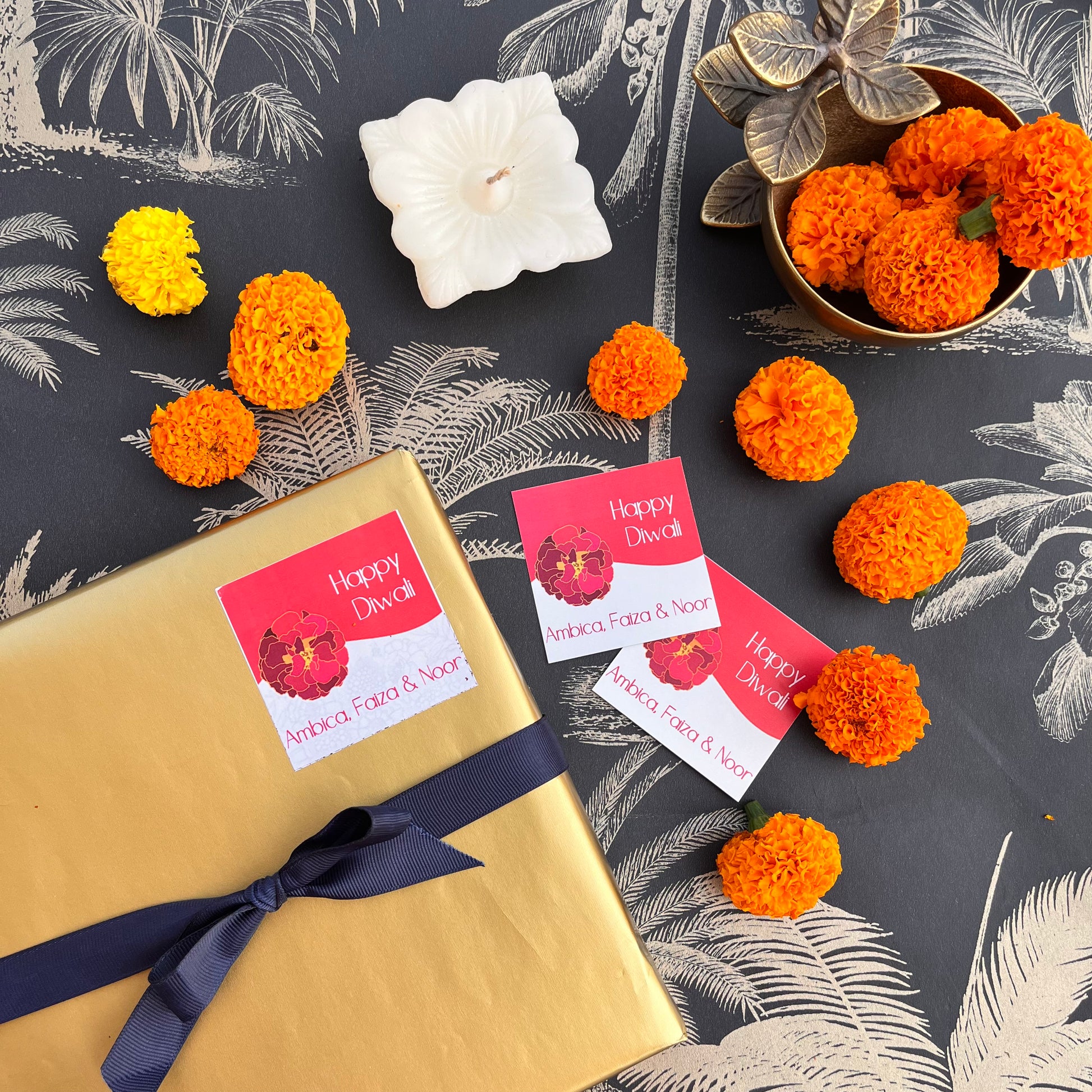 Gift tags with 'Happy Diwali' and 'Happy New Year' text, presented on a gift wrapped in gold paper, alongside orange decorations and a candle.
